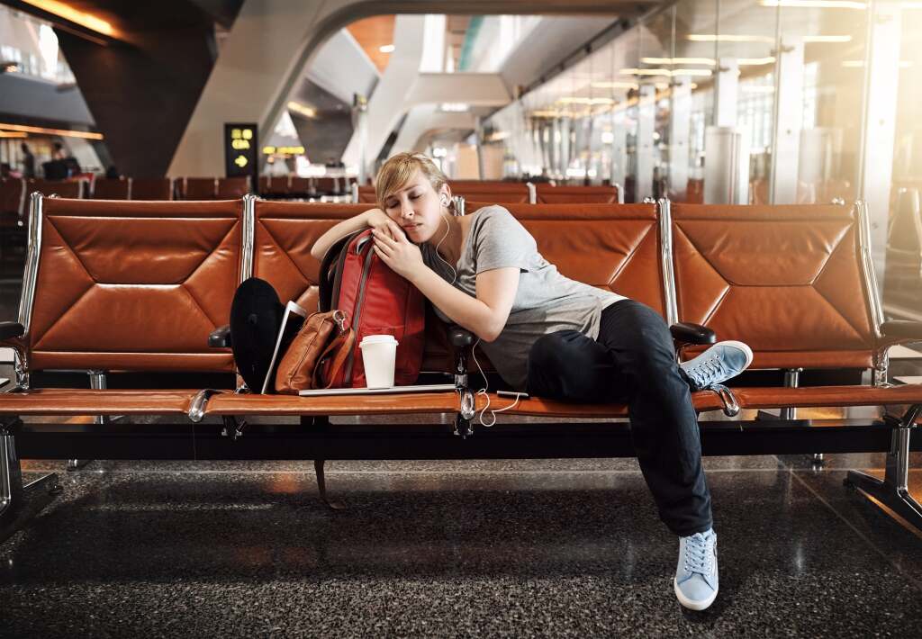 Co to jest jet lag, jakie daje objawy, jak sobie z nim poradzić? Kobieta z walizką na lotnisku obserwuje odlatujący samolot.